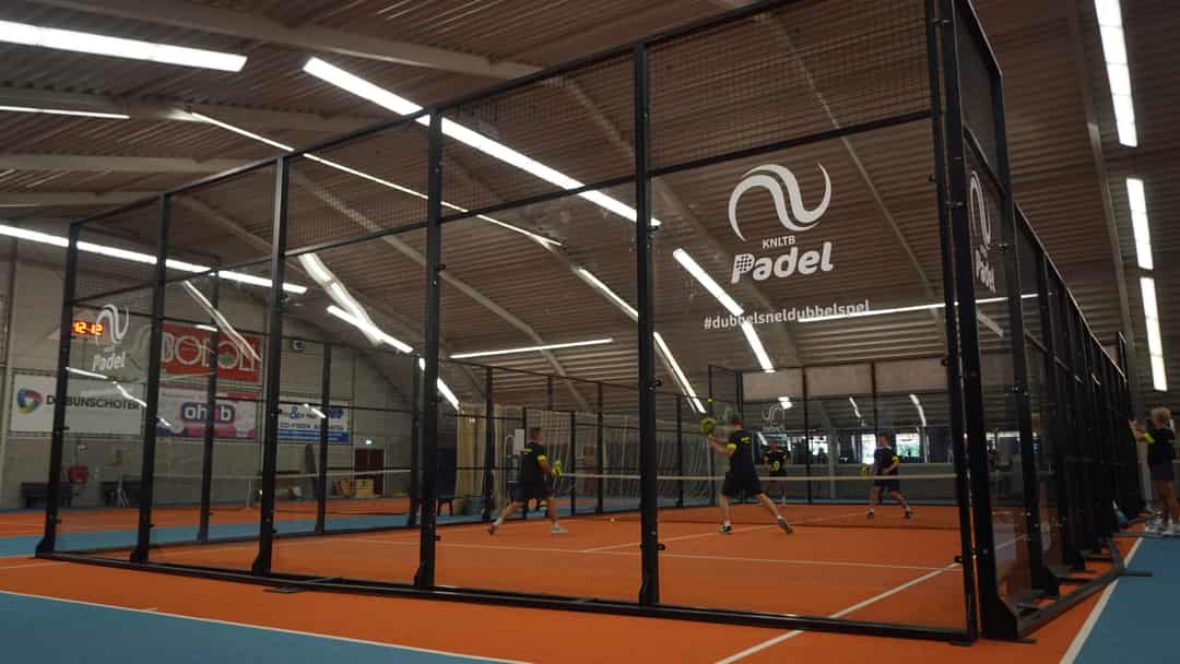 Spelers in actie op een indoor padelbaan met KNLTB Padel-branding op de glaswand