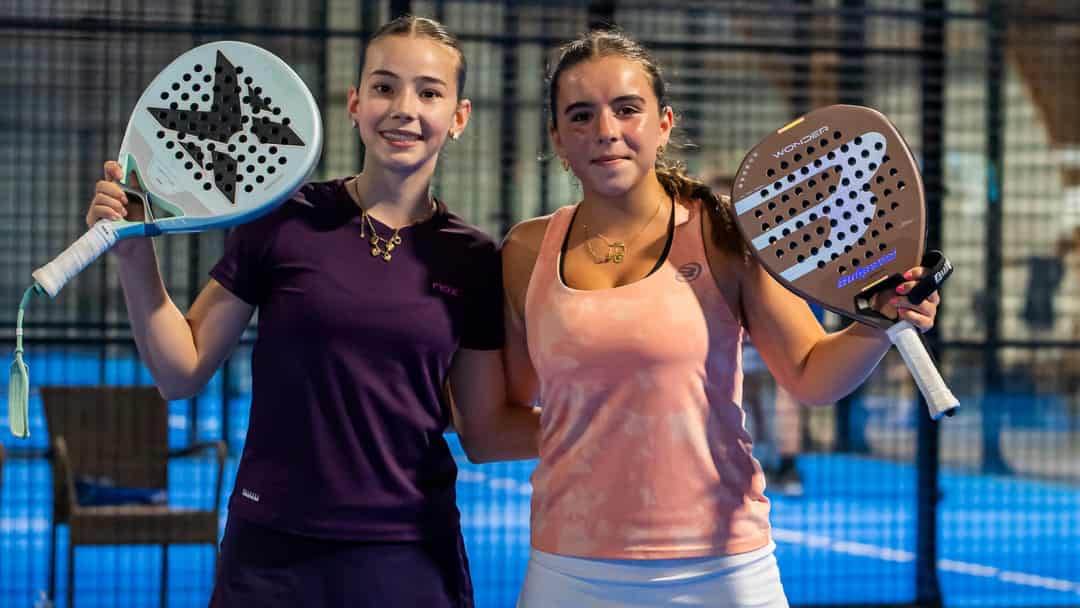 Twee jeugdspeelsters poseren met hun padelrackets op een indoorbaan tijdens een FIP Promises-toernooi