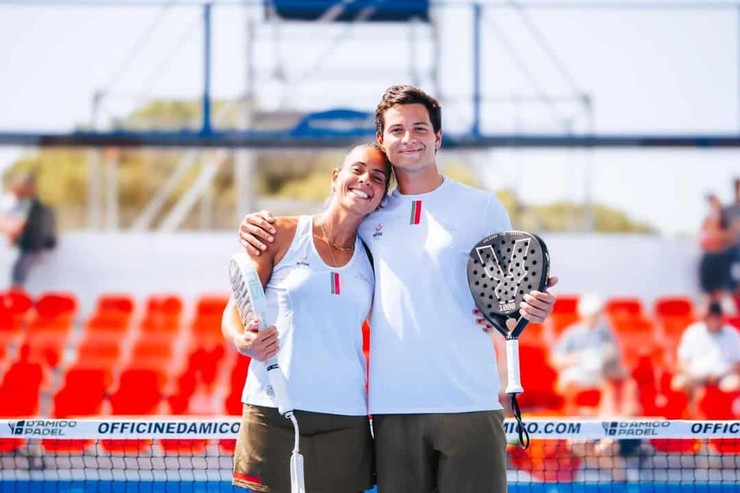 Sofia en Pedro Araujo met de arm om elkaar heen bij het net op de outdoorbaan in Taranto