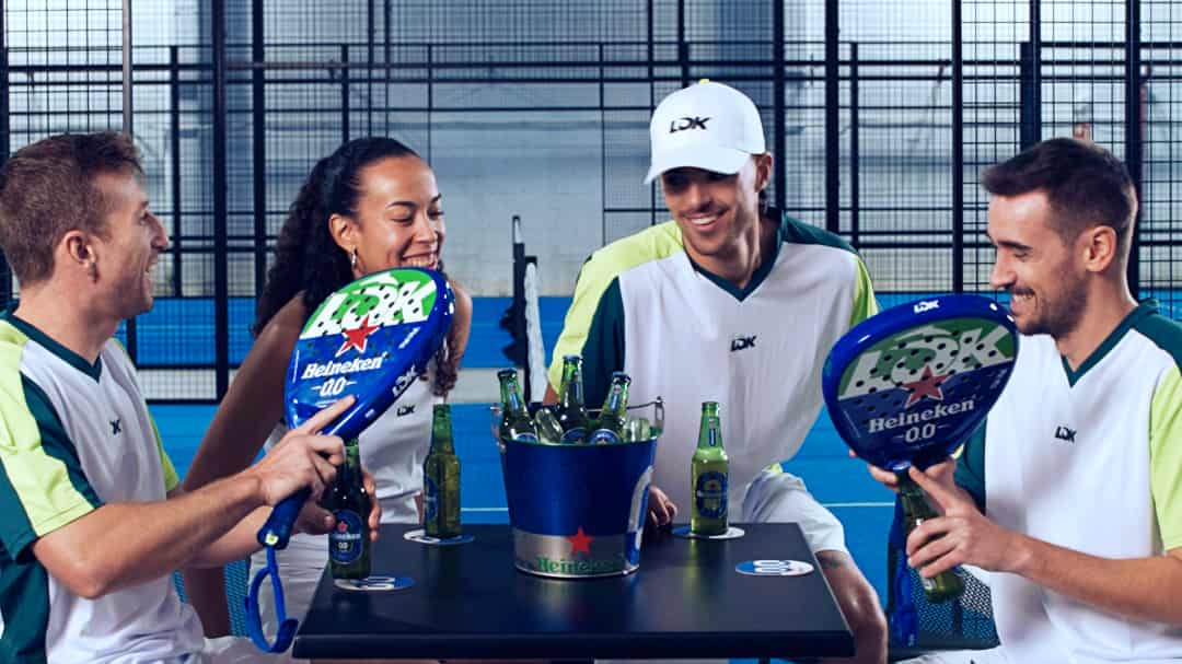 Vier padelspelers met Heineken 0.0 x LÕK rackets en flesjes naast een padelbaan