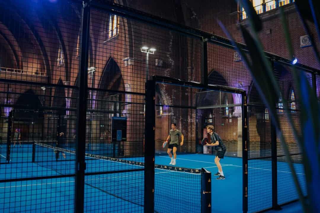 Twee padelspelers op een baan in de Sint-Jozefkerk in Arnhem met gotische bogen op de achtergrond