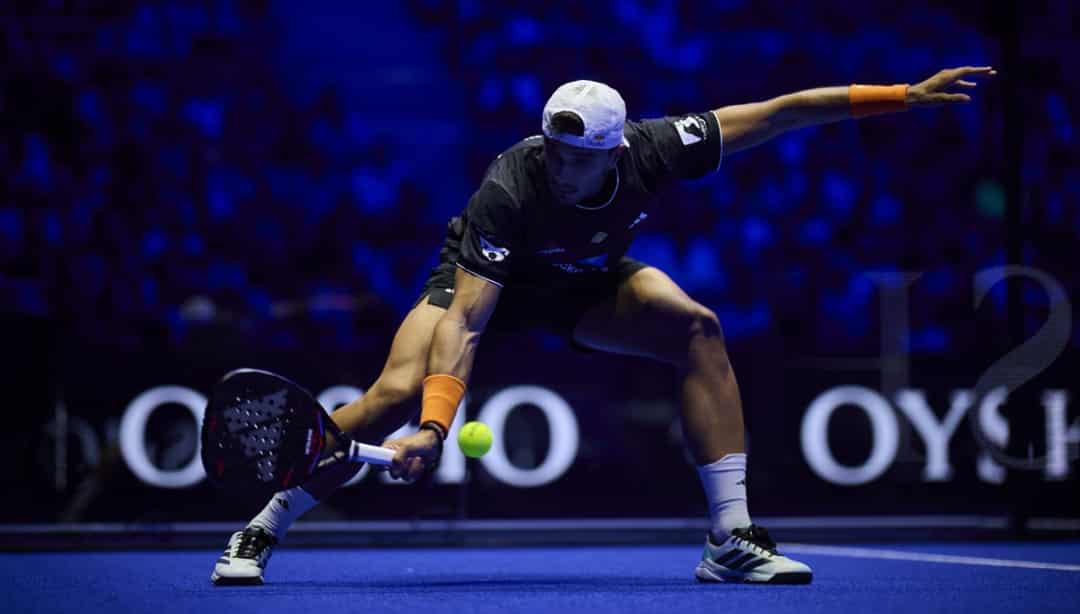 Speler strekt zich uit voor een lage volley op de blauwe baan tijdens het Premier Padel P1 in Madrid