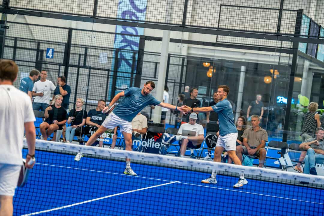 Twee padelspelers geven elkaar een high five op een indoorbaan van Peakz Padel met publiek langs de kant