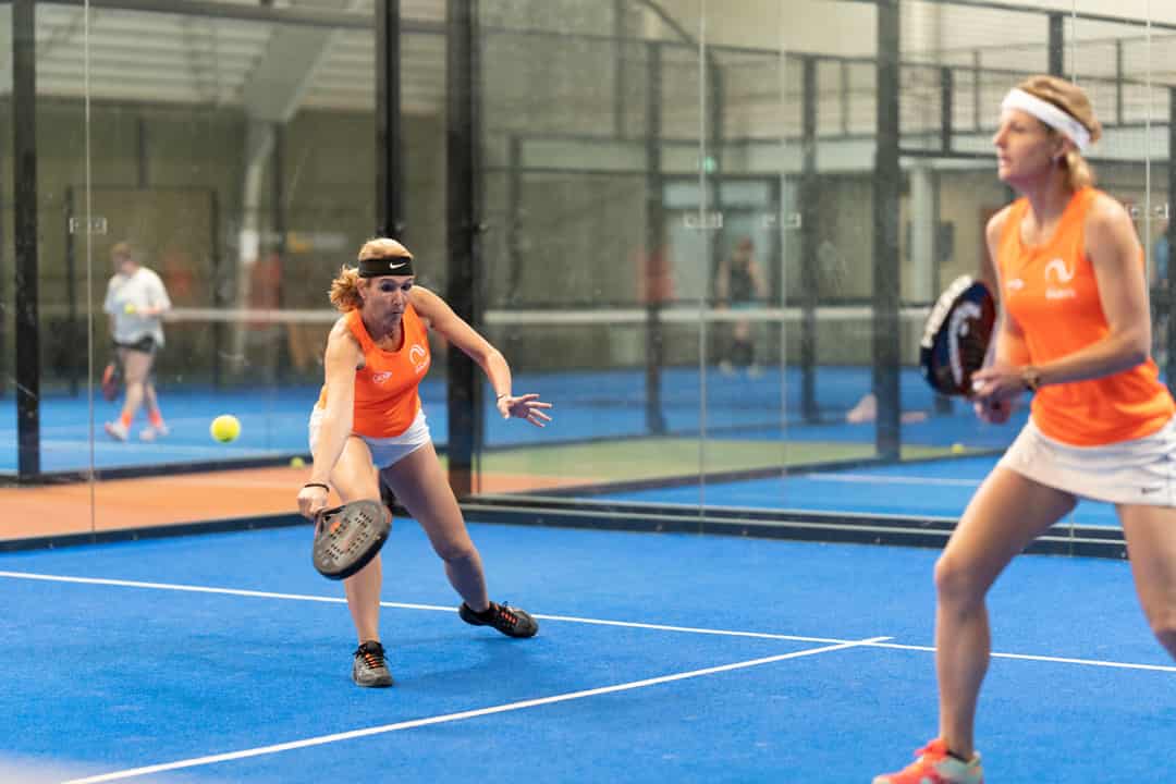 Twee speelsters in oranje tenue in actie tijdens een wedstrijd van het Nederlandse seniorenpadelteam