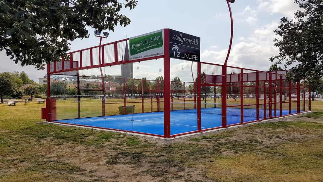 Buitenpadelbaan met glaswanden in een open omgeving nabij bebouwing