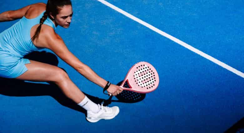 Speelster slaat een lage bal met de roze Wilson Blade V4 LS op een blauwe padelbaan