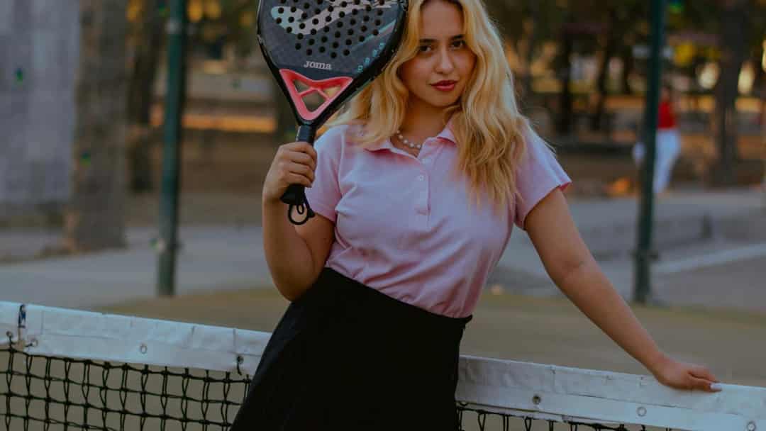 Vrouw in roze polo en zwart rokje met padelracket op een padelbaan