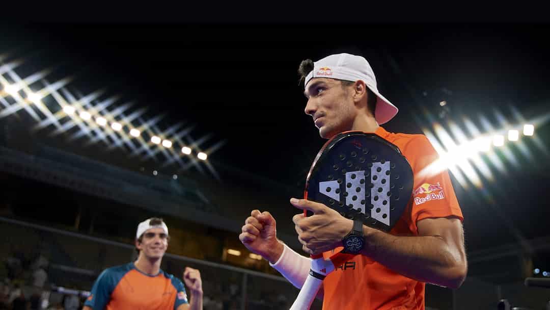 Twee padelspelers in Red Bull-outfit vieren een punt op een Premier Padel-baan met stadionverlichting