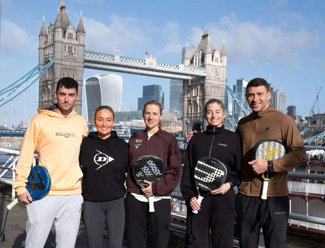 Vijf padelspelers met rackets poseren voor Tower Bridge en de skyline van Londen