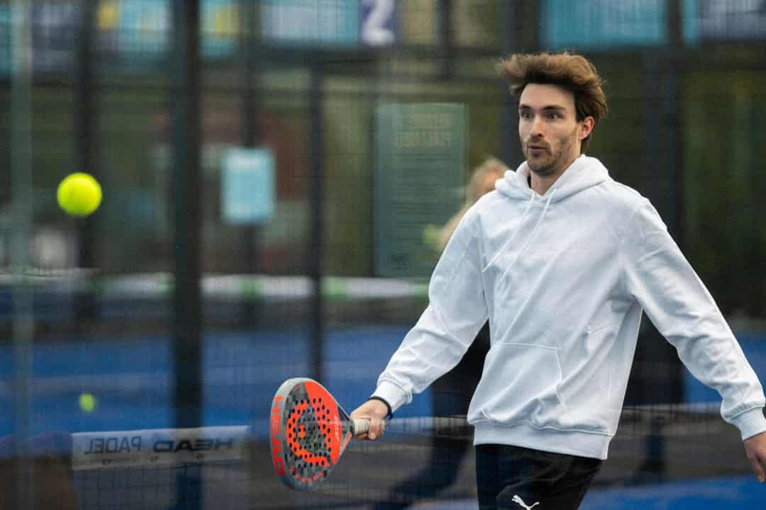 Speler slaat een bal terug op een outdoor padelbaan bij kil, grijs weer in Nederland
