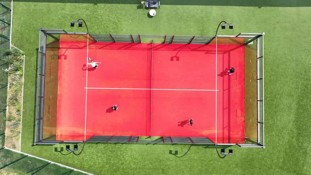 Dronefoto van een padelbaan met vier spelers in actie op een rood court